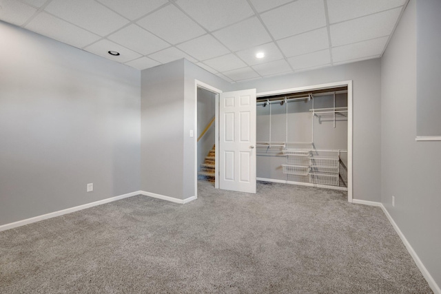 unfurnished bedroom with a closet, a paneled ceiling, baseboards, and carpet floors