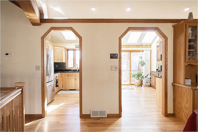 corridor featuring light wood finished floors, plenty of natural light, visible vents, and arched walkways