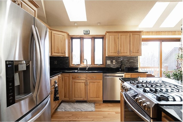 kitchen with light wood-style flooring, a sink, appliances with stainless steel finishes, tasteful backsplash, and dark countertops