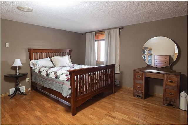 bedroom with light wood-style floors, visible vents, a textured ceiling, and baseboards