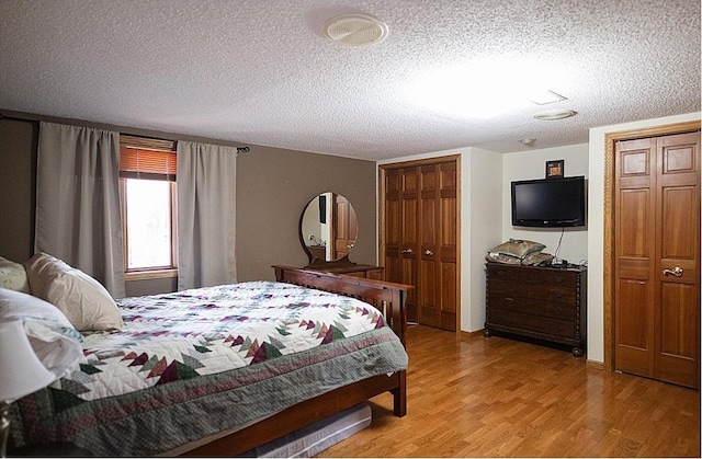 bedroom featuring a textured ceiling, light wood finished floors, and two closets