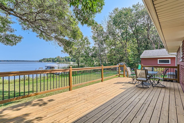 deck with outdoor dining space, a water view, and a lawn