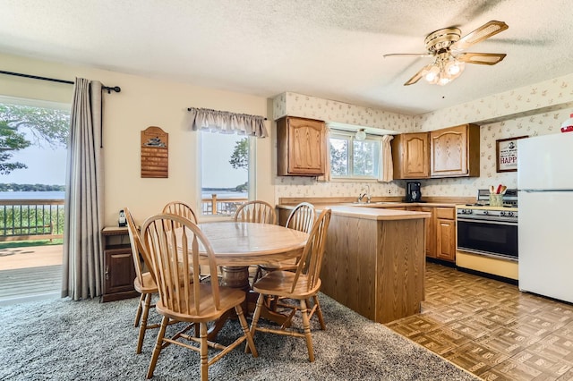 kitchen with range with gas stovetop, freestanding refrigerator, a textured ceiling, and wallpapered walls