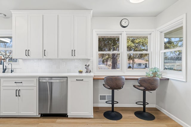 kitchen featuring white cabinets, light countertops, decorative backsplash, baseboards, and dishwasher