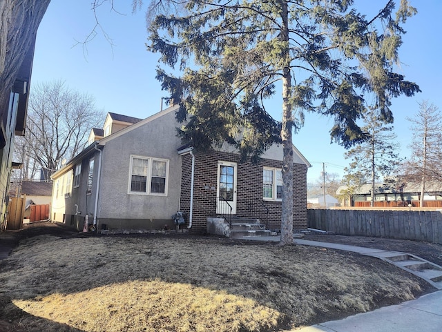 view of side of home featuring brick siding, fence, and stucco siding