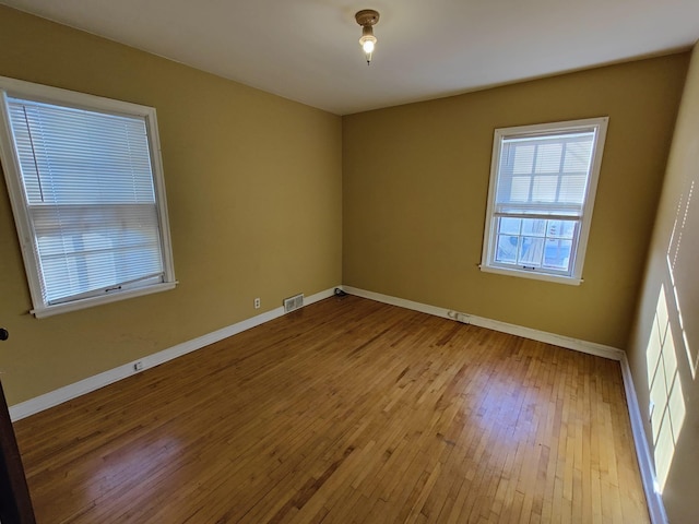 spare room with wood-type flooring, visible vents, and baseboards