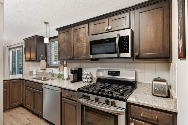 kitchen with tasteful backsplash, light stone countertops, stainless steel appliances, dark brown cabinets, and a sink