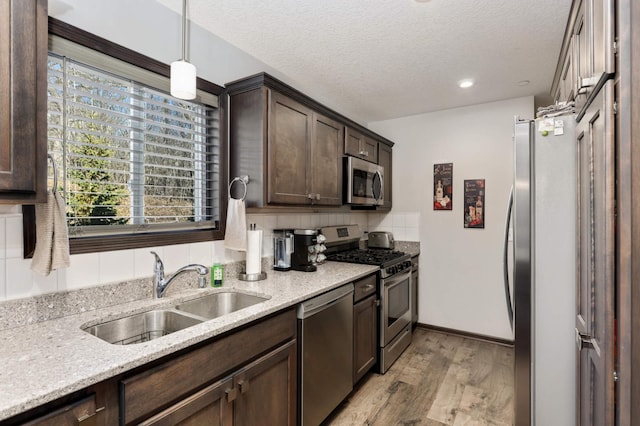 kitchen with dark brown cabinetry, a sink, appliances with stainless steel finishes, light stone countertops, and light wood finished floors