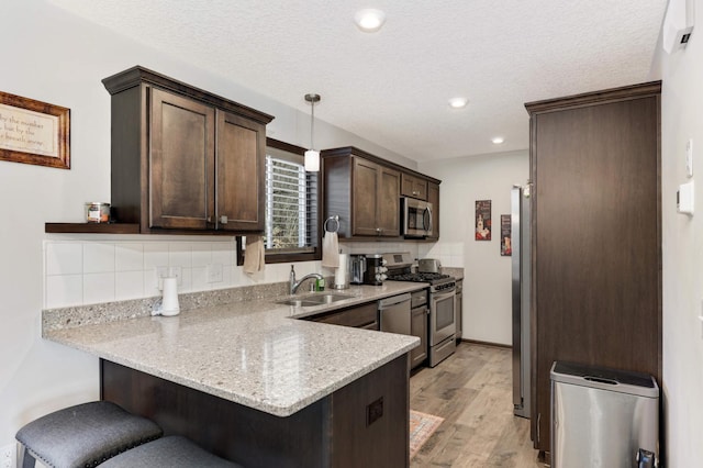 kitchen featuring dark brown cabinetry, a peninsula, a sink, appliances with stainless steel finishes, and a kitchen bar