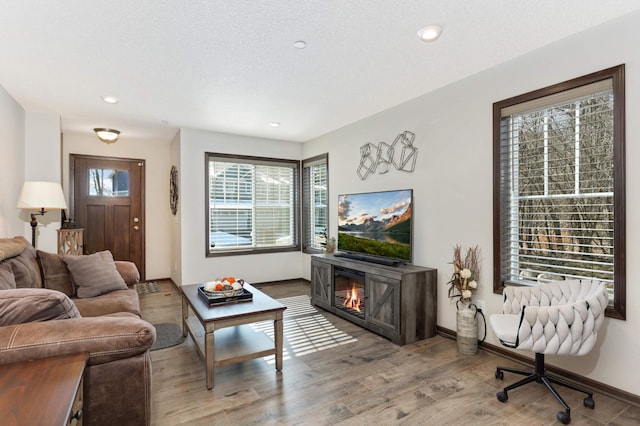 living area with baseboards, recessed lighting, a glass covered fireplace, and light wood-style floors