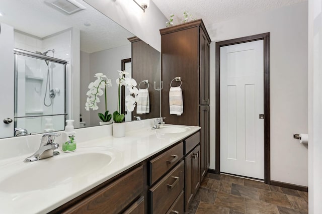 bathroom with a stall shower, stone finish flooring, a textured ceiling, and a sink