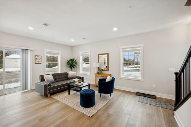 living area with a healthy amount of sunlight, light wood-style floors, baseboards, and stairway