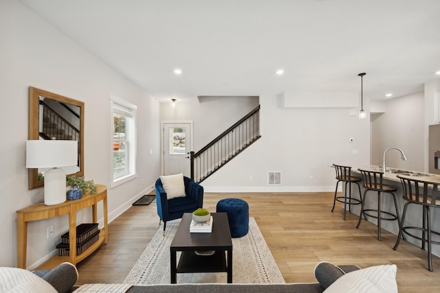 living room with stairs, light wood-type flooring, visible vents, and recessed lighting