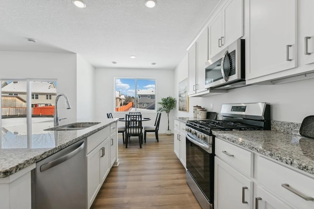 kitchen with light stone counters, light wood finished floors, a sink, stainless steel appliances, and a textured ceiling