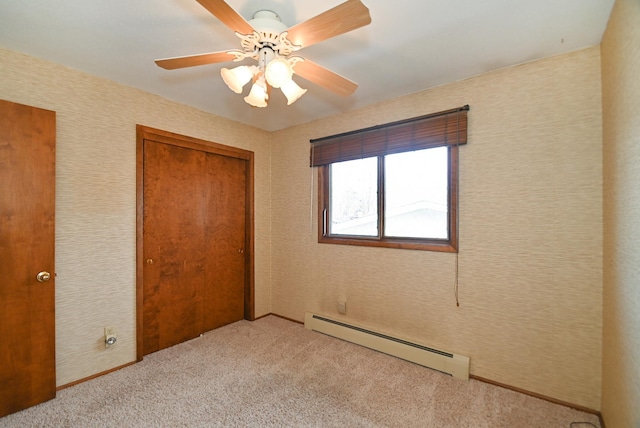 unfurnished bedroom with wallpapered walls, ceiling fan, a closet, a baseboard heating unit, and light colored carpet