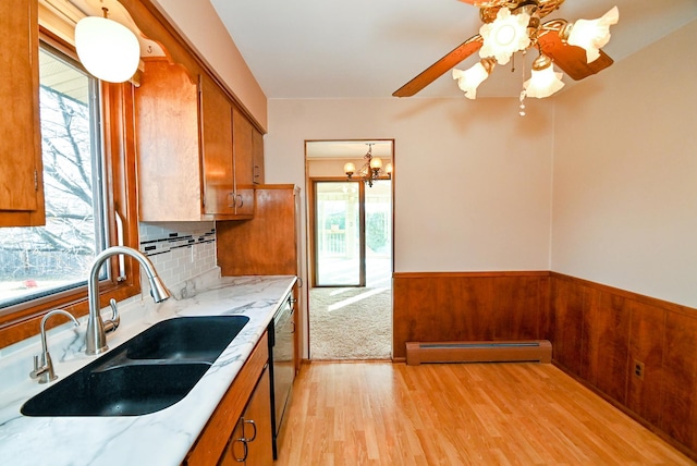 kitchen with brown cabinetry, baseboard heating, wainscoting, and a sink