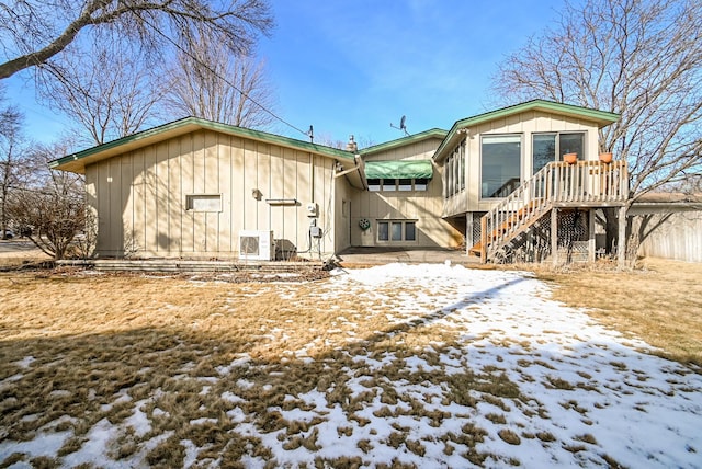 snow covered back of property featuring ac unit, board and batten siding, and stairs