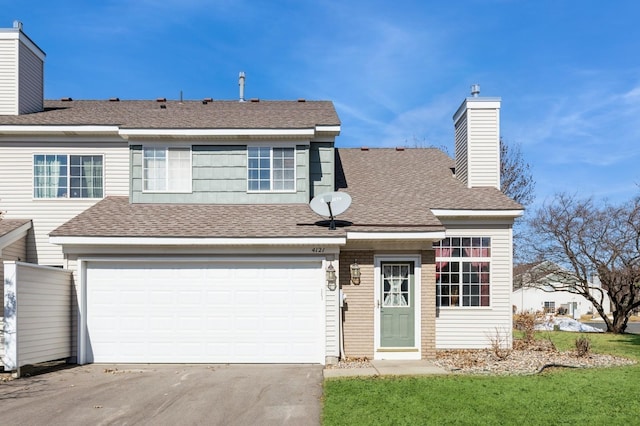 view of front of house with concrete driveway, roof with shingles, a front yard, a chimney, and a garage