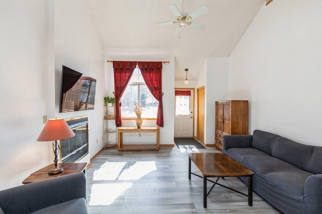 living room featuring a glass covered fireplace, wood finished floors, baseboards, and a ceiling fan