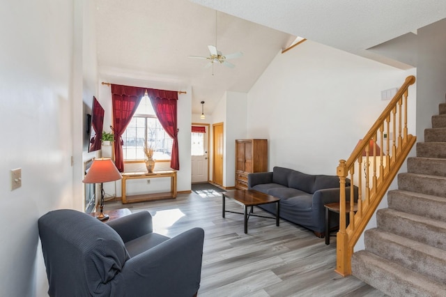 living room featuring stairs, a ceiling fan, wood finished floors, and high vaulted ceiling