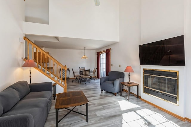 living room featuring wood finished floors, a high ceiling, a glass covered fireplace, and stairs