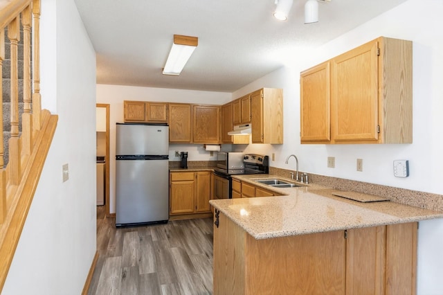 kitchen featuring light stone countertops, a peninsula, a sink, under cabinet range hood, and appliances with stainless steel finishes