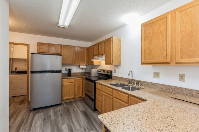 kitchen featuring under cabinet range hood, a sink, wood finished floors, stainless steel appliances, and washer / dryer