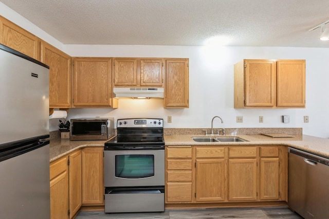 kitchen featuring under cabinet range hood, a textured ceiling, stainless steel appliances, and a sink