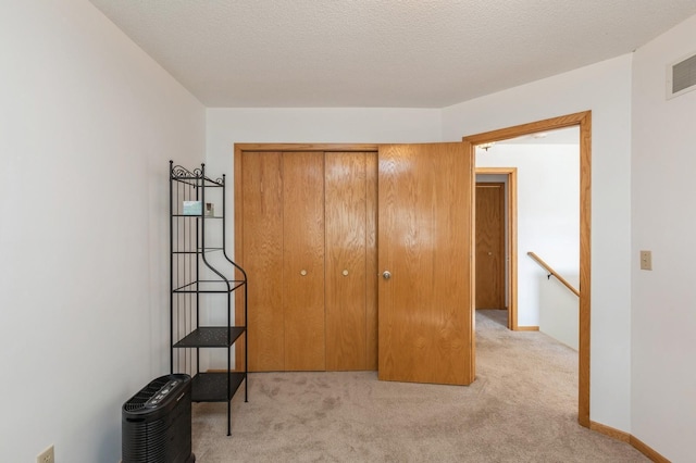 bedroom featuring visible vents, baseboards, light colored carpet, a closet, and a textured ceiling