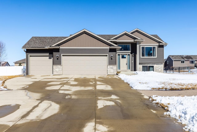 view of front of home with an attached garage, stone siding, driveway, and fence