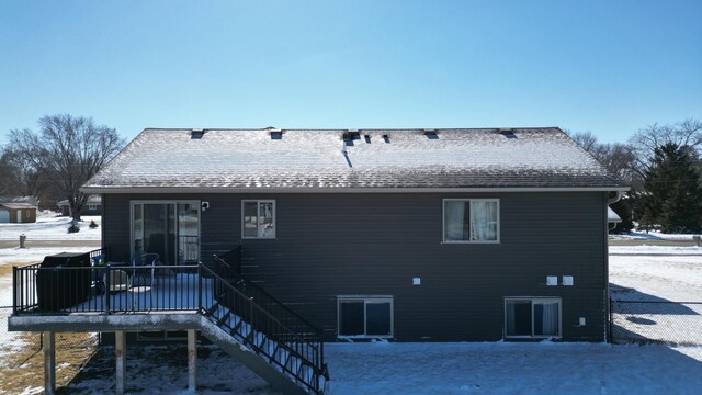 snow covered rear of property featuring a shingled roof, a deck, and stairs