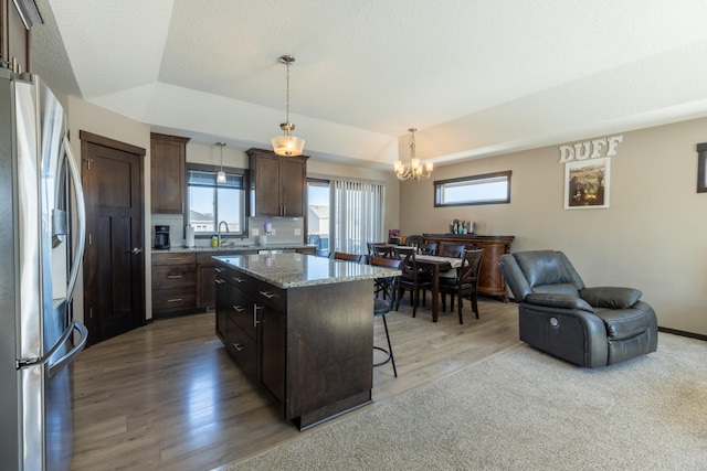 kitchen with dark brown cabinetry, stainless steel fridge with ice dispenser, open floor plan, a center island, and a kitchen bar