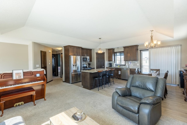 living room featuring lofted ceiling, a raised ceiling, a notable chandelier, and light wood-style flooring