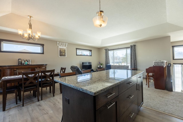 kitchen with light stone counters, pendant lighting, a raised ceiling, a kitchen island, and light wood-type flooring