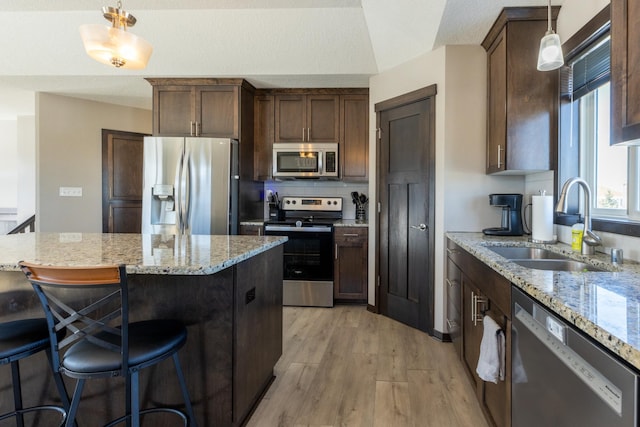 kitchen featuring light wood-style flooring, appliances with stainless steel finishes, light stone countertops, pendant lighting, and a sink