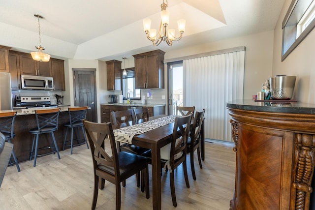 dining space featuring a notable chandelier, a tray ceiling, vaulted ceiling, and light wood-style floors