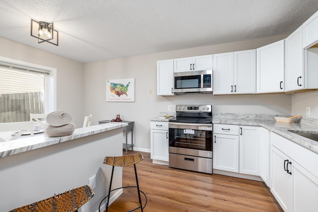 kitchen with light stone counters, appliances with stainless steel finishes, a textured ceiling, white cabinetry, and light wood-type flooring