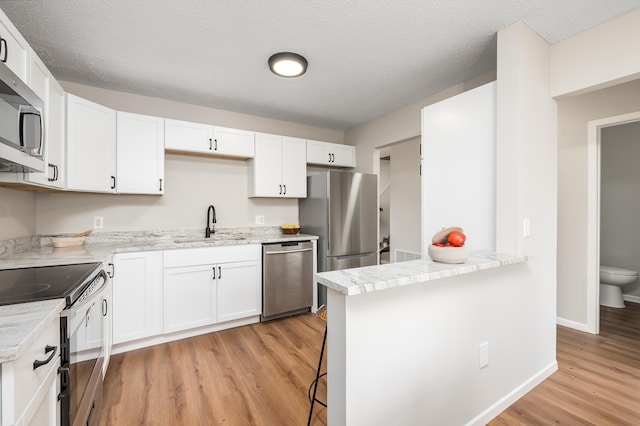 kitchen with white cabinets, stainless steel appliances, light wood-type flooring, and a sink