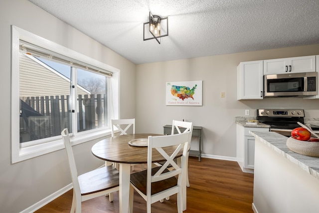 dining space with a textured ceiling, baseboards, and dark wood-style flooring