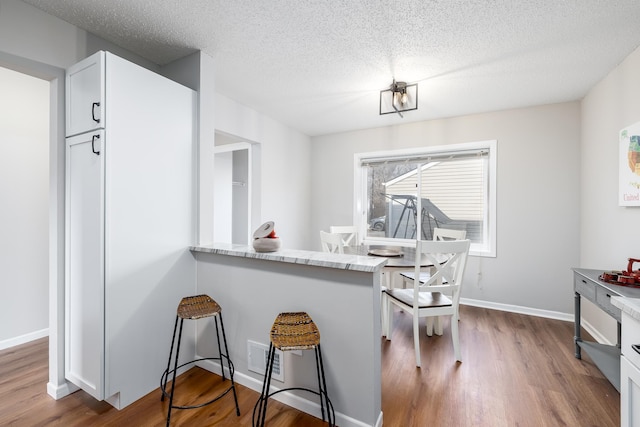 kitchen with white cabinets, light stone countertops, baseboards, and dark wood-style flooring