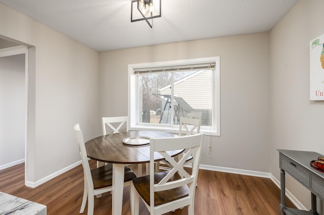 dining space featuring a textured ceiling, baseboards, and wood finished floors