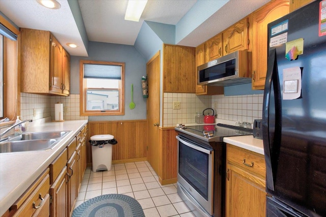 kitchen featuring a wainscoted wall, appliances with stainless steel finishes, brown cabinets, wood walls, and a sink