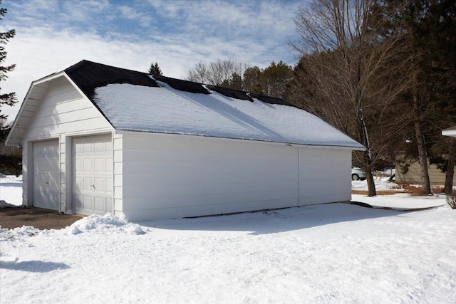 snow covered property with a shingled roof and a detached garage