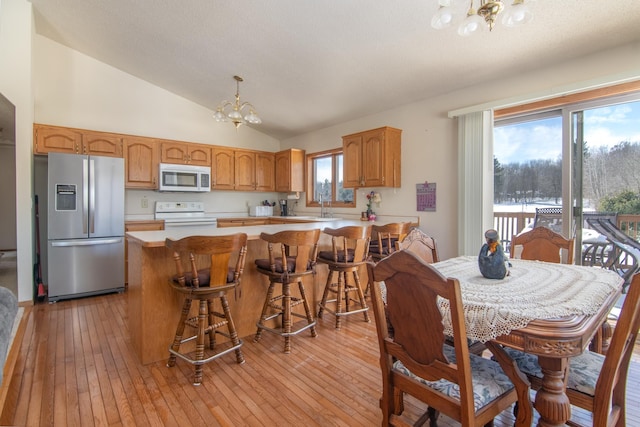 kitchen with white appliances, light wood-style flooring, vaulted ceiling, light countertops, and a notable chandelier