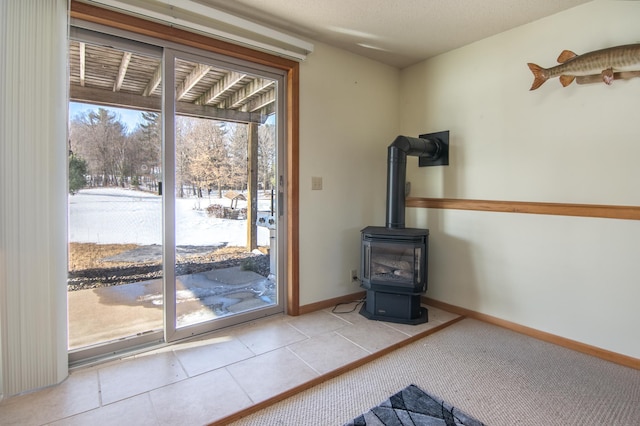 entryway with carpet flooring, tile patterned flooring, a wood stove, and baseboards