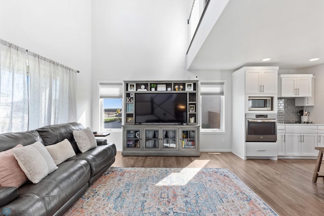 living room featuring a high ceiling, recessed lighting, light wood-style flooring, and baseboards