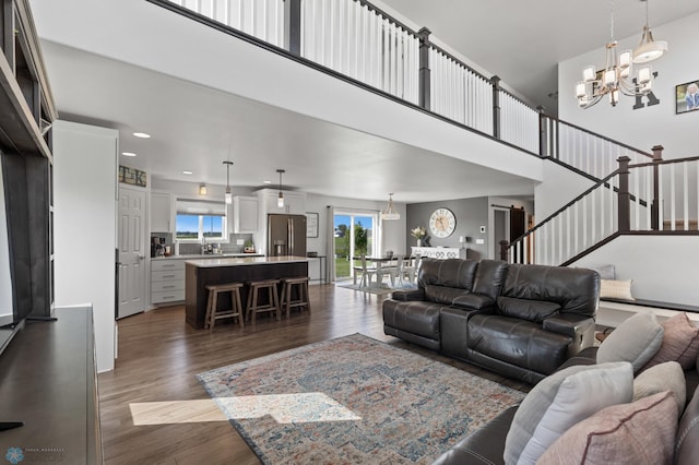 living area with a chandelier, stairway, dark wood finished floors, and a towering ceiling