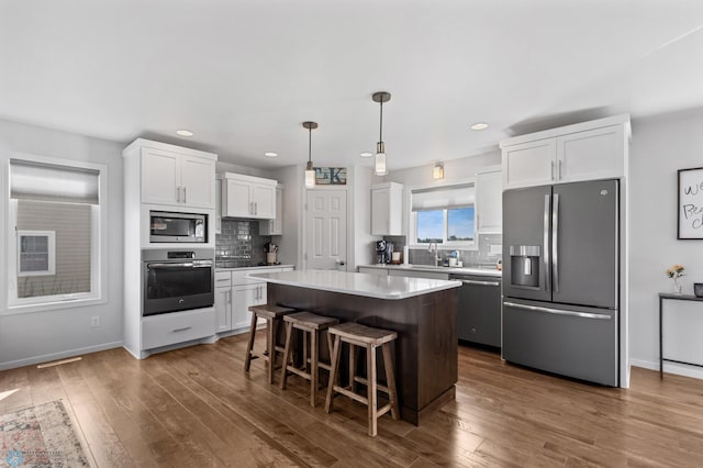 kitchen featuring a center island, a breakfast bar, dark wood finished floors, light countertops, and appliances with stainless steel finishes