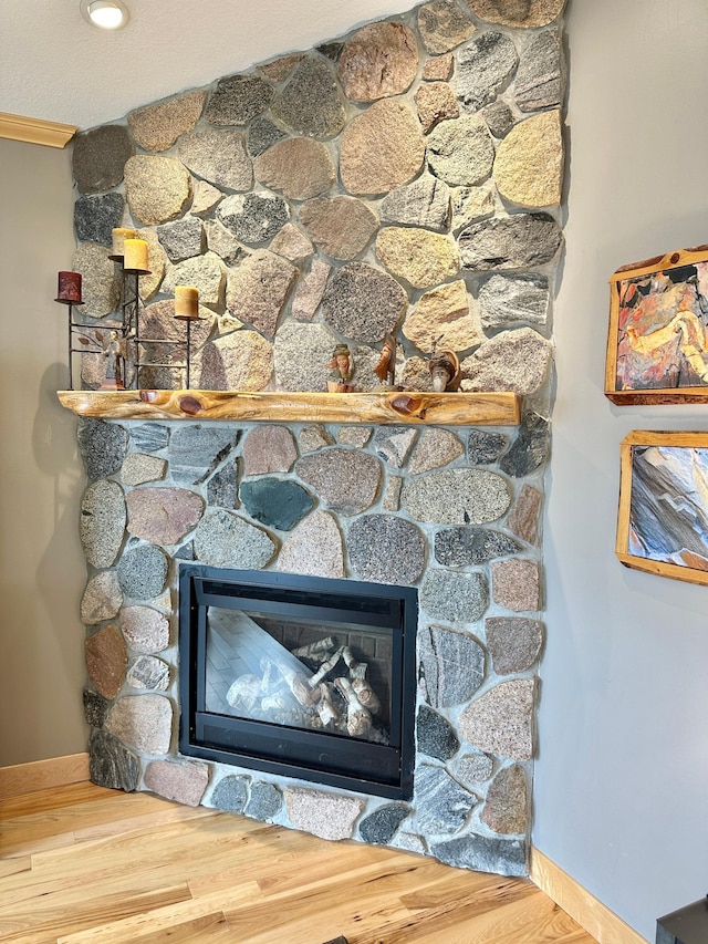 details with a stone fireplace, wood finished floors, and baseboards