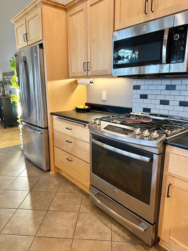 kitchen featuring light tile patterned floors, dark countertops, stainless steel appliances, light brown cabinets, and backsplash